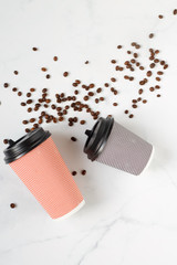 two paper coffee glasses lie on a white table with scattered coffee beans close up flat lay