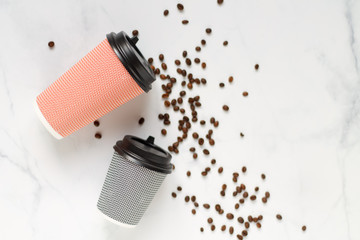 two paper coffee glasses lie on a white table with scattered coffee beans close up flat lay