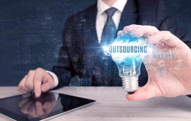 Businessman holding a light bulb with OUTSOURCING inscription, new business concept