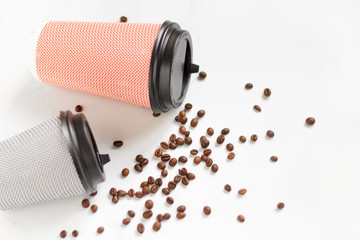 two paper coffee glasses lie on a white table with scattered coffee beans close up flat lay