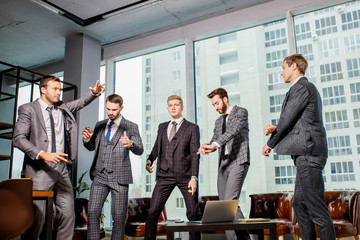 dancing happy business men after meeting in office, enjoy work together, celebrating at work. panoramic window in the background