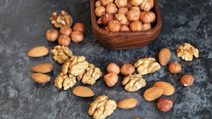 different types of nuts around a wooden dish with hazelnuts on a black background