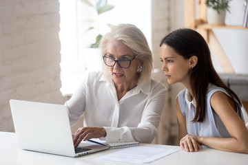 Mature woman mentor explain intern corporate application seated at desk