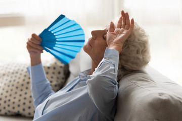 Exhausted older woman feeling unwell, suffering from heat, waving fan
