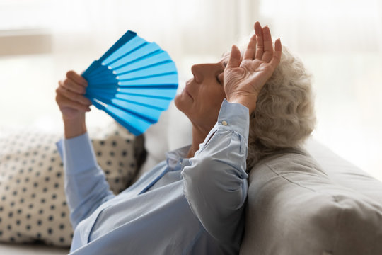 Exhausted older woman feeling unwell, suffering from heat, waving fan