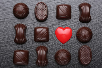 Red heart and chocolate candies on black slate stone. Valentines day greeting card.