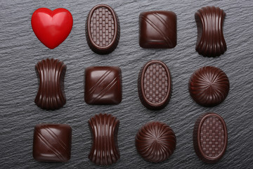 Red heart and chocolate candies on black slate stone. Valentines day greeting card.