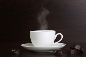 Cup of coffee and chocolate candies on wooden background