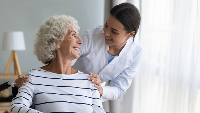 Smiling Caregiver Caring About Happy Disabled Older Woman In Wheelchair