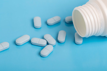 Blue pills and white plastic medicine bottle on blue background