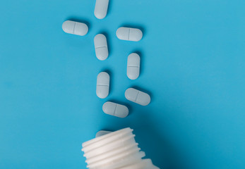 Blue pills and white plastic medicine bottle on blue background