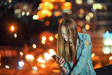 Teen girl on night cityscape background holding a phone in hand chatting