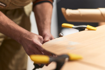 detail of hands smoothing the edge of a wooden board with a Dremel machine. selective focus with blurry background