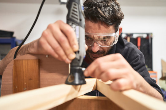 portrait of young man with safety glasses working with a Dremel tool