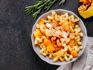 Fusilli pasta with pumpkin, rosemary and brie cheese. Idea recipe pasta. Vegetarian food. Homemade pasta dish in gray bowl over black concrete background. Copy space. Top view or flat lay.