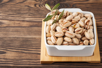 pistachios and leaves in a white plate on a wooden stand and background, copy space