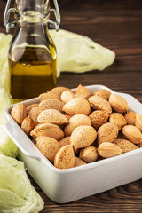inshell almonds on a wooden background and a bottle of almond oil