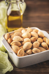 inshell almonds in a white bowl on a wooden background and a bottle of almond oil