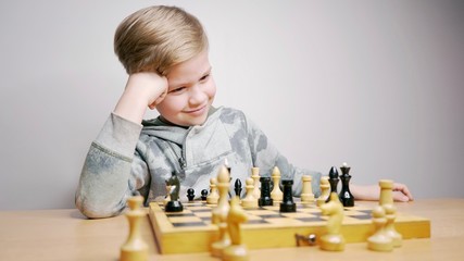 Happy beautiful boy playing chess. Caucasian child thinks while playing chess boardgame. White background                             