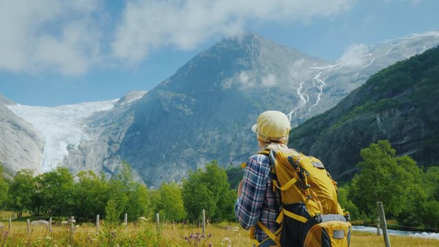 A young woman with a backpack walks along the road between the mountains, travels through the picturesque places of Norway
