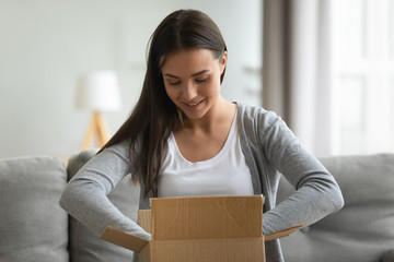 Smiling woman unpacking parcel at home, sitting on couch