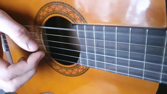Enumeration of strings on an acoustic guitar of light brown color. Playing the instrument. Men's hands.
