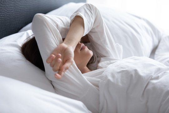 Sleepless young woman suffering from insomnia, covering eyes with hands