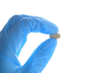 Hand holds a multivitamin complex pill horizontally. Wearing blue medical nitrile glove.