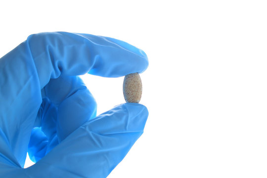 Hand Holds A Multivitamin Complex Pill Horizontally. Wearing Blue Medical Nitrile Glove.