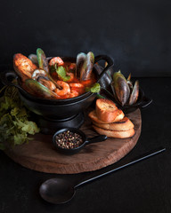French fish soup Bouillabaisse with seafood, salmon fillet, shrimp on a black background....