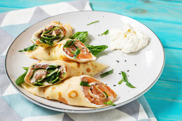 Delicious breakfast or brunch - crepes with smoked salmon, spinach and sour cream on wood background.