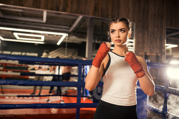 Fototapeta premium Portrait of strong muscular fitness woman ready to fight in gym, wearing red bandage on hands and sportive wear