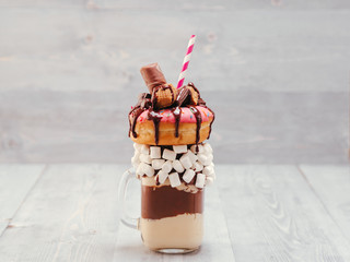 Chocolate and donuts extreme milkshake with marshmallow and other sweets in mason jar on gray...