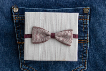 A little present in craft paper and a brown ribbon in a pocket of blue jeans. Holidays content