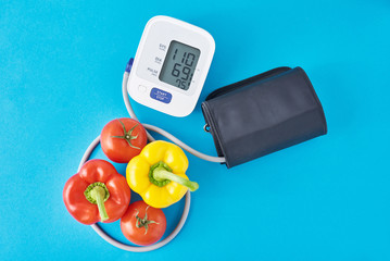 Digital blood pressure monitor and fresh vegetables on a blue background. Healthcare concept
