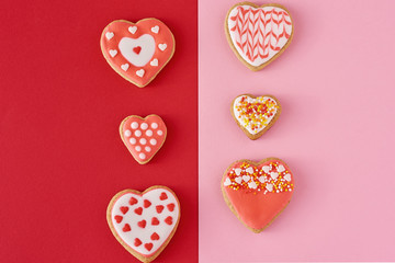 Fototapeta premium Decorated heart shape cookies on a colored red and pink background, top view