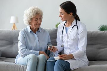 Friendly doctor checking older woman blood pressure at home