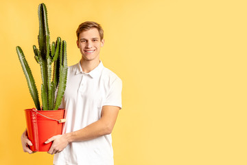 portrait of young caucasian man in white t-shirt working in delivery service, holding green plant...