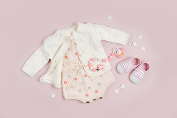 Pastel knitted romper with jumper,  baby shoes and pacifier. Cute set of baby clothes and accessories on pink background. Fashion newborn bodysuit. Flat lay, top view