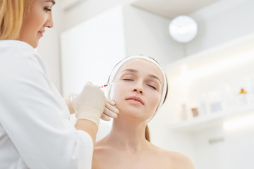 master cosmetologist makes botox injections into the eyebrow of a beautiful young woman client. The concept of rejuvenating aesthetic procedures