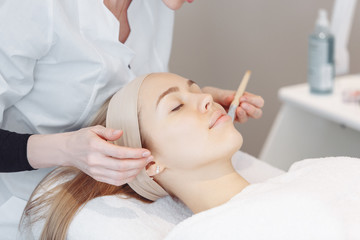 Beautician smears the skin with a rejuvenating serum of the face of her client woman with a brush. The concept of modern anti-aging procedures in the beauty salon