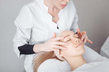 Unknown masseuse beautician doing a face massage to her client a beautiful young woman. Skin care concept