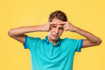 Fototapeta na wymiar Cosmetology, Dermatology and acne. Caucasian teenager in a blue t-shirt, painfully squeezes out a pimple on his forehead. Yellow background. Copy space