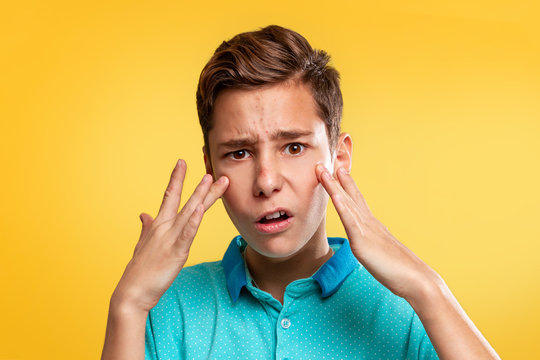 Cosmetology, Dermatology and acne. A Caucasian teenager in a blue t-shirt is upset about the appearance of acne. Yellow background. Copy space