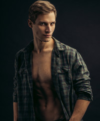 young caucasian man with muscular strong body opened torso, checkered casual shirt on him, he looks side isolated over black background