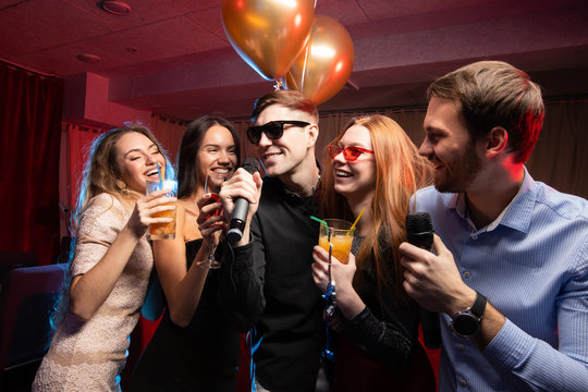 Group Of Beautiful Young Caucasian People, Guys And Ladies Chilling Out In Karaoke Bar, Have Fun, Spend Free Time Together In Karaoke, Singing And Communicating