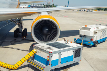Big modern commercial plane parked on airport runway and connected to ground supply power unit....