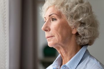 Close up thoughtful older woman looking out window at home