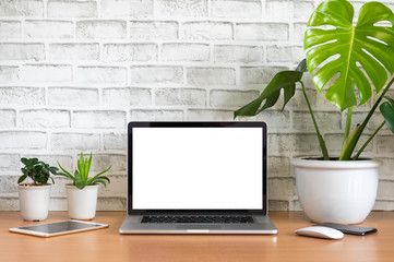 Blank screen of Laptop computer with tablet, mobile phone, mouse and monstera plant pots on wooden...