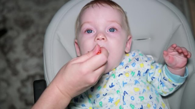 A small child, a boy, is spoon-fed at home. A newborn plays and smiles while lying in a child's chair. The concept of a happy childhood.
